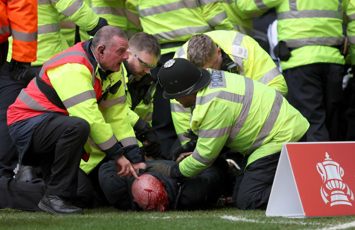 Police officers and a security steward pictured restraining an injured fan following crowd violence during an FA Cup game between West Brom and Wolves in January 2024
